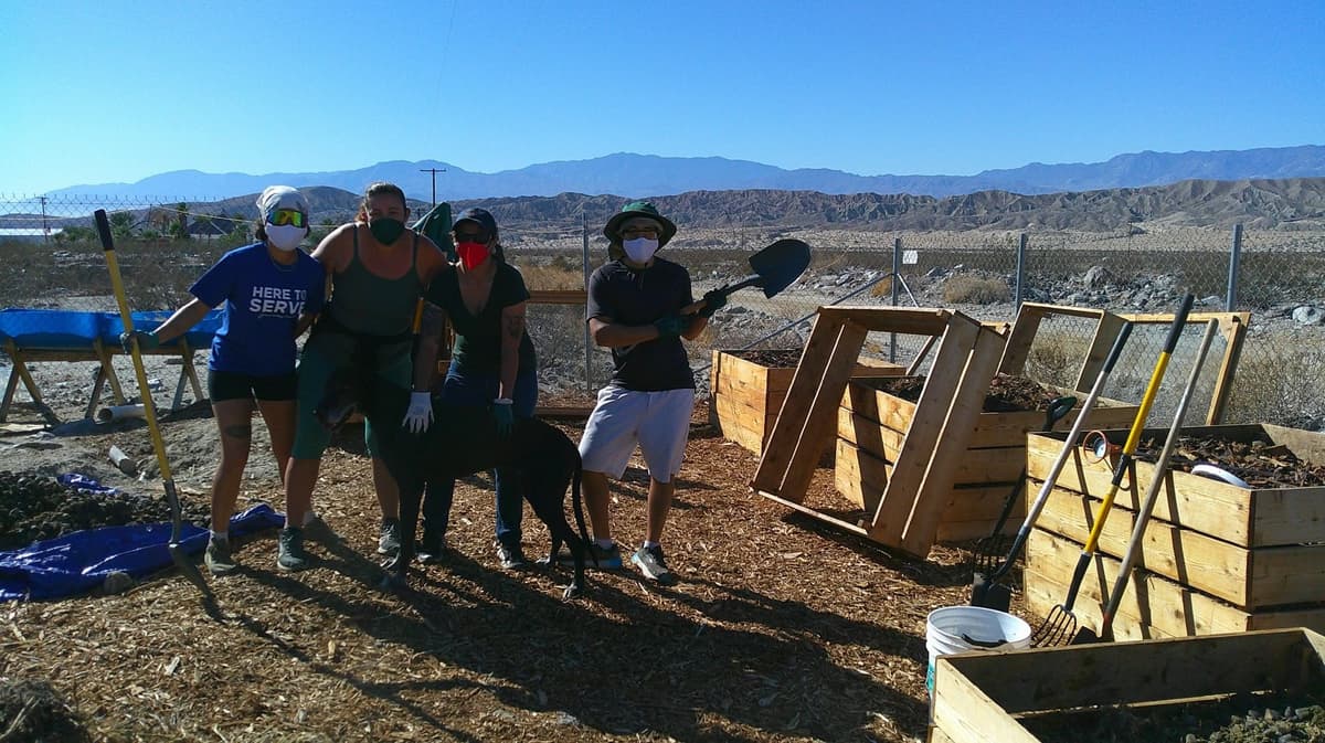 A group of volunteers posing with shovels in front of compost piles